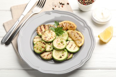 Photo of Delicious fried courgette slices with lemon and parsley served on white wooden table, closeup