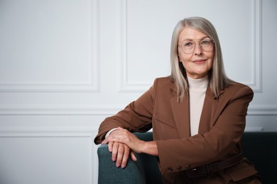 Photo of Portrait of beautiful senior woman on sofa near white wall. Space for text