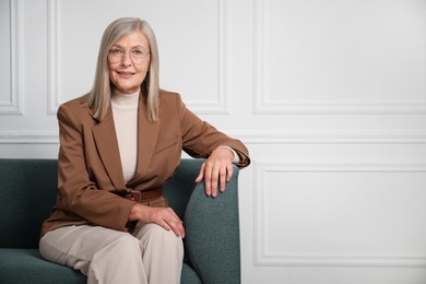 Photo of Portrait of beautiful senior woman on sofa near white wall. Space for text