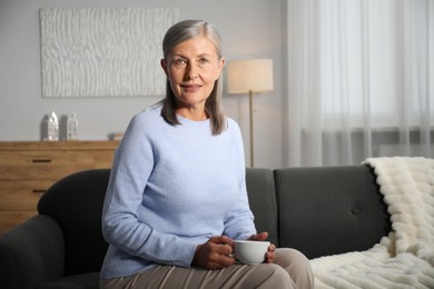 Photo of Senior woman having tea on sofa at home