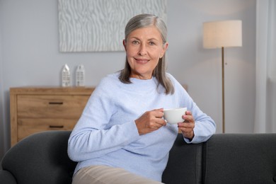 Photo of Senior woman having tea on sofa at home