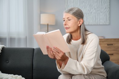 Photo of Beautiful senior woman reading book on sofa at home