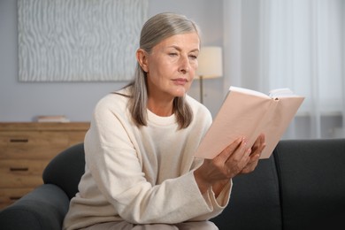Photo of Beautiful senior woman reading book on sofa at home