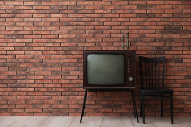 Photo of Retro TV on stand and black chair near red brick wall, space for text. Used stuff