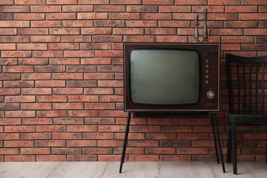 Photo of Retro TV on stand and black chair near red brick wall, space for text. Used stuff
