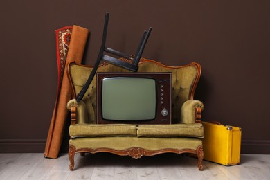 Photo of Retro TV on sofa, chair, suitcase and carpet near brown wall. Used stuff