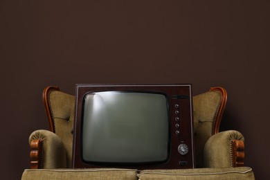 Photo of Retro TV on sofa near brown wall, space for text. Used stuff