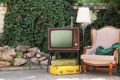 Photo of Retro TV on stand, armchair and other used stuff outdoors