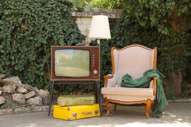 Photo of Retro TV on stand, armchair and other used stuff outdoors