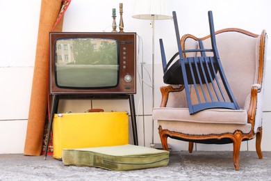 Photo of Retro TV on stand, armchair and other used stuff near white wall outdoors