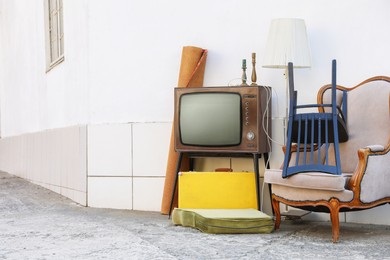 Photo of Retro TV on stand, armchair and other used stuff near white wall outdoors. Space for text