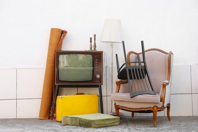 Photo of Retro TV on stand, armchair and other used stuff near white wall outdoors