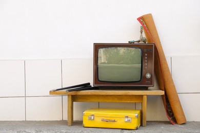 Photo of Retro TV on table, carpet and suitcase near white wall outdoors. Used stuff