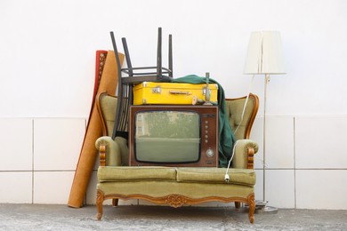 Photo of Retro TV on sofa and other used stuff near white wall outdoors