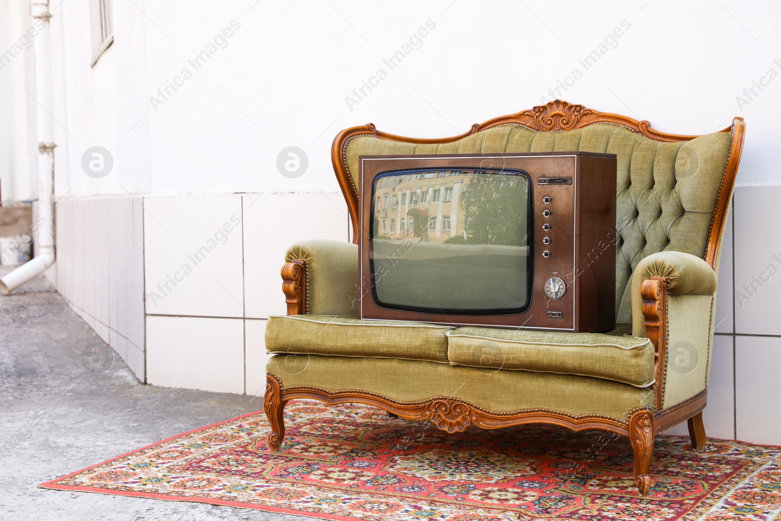 Retro TV on sofa and carpet near white wall outdoors. Used stuff Photo of Retro TV on sofa and carpet near white wall outdoors. Used stuff