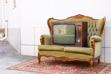 Photo of Retro TV on sofa and carpet near white wall outdoors. Used stuff