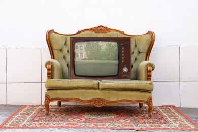 Photo of Retro TV on sofa and carpet near white wall outdoors. Used stuff
