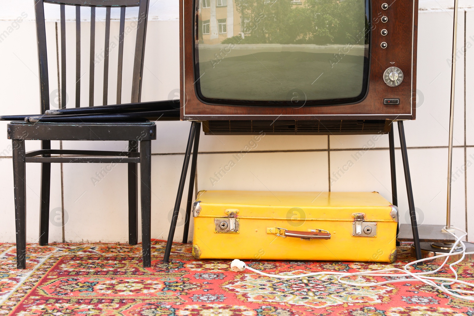 Retro TV on stand, suitcase and black chair near white wall. Used stuff Photo of Retro TV on stand, suitcase and black chair near white wall. Used stuff