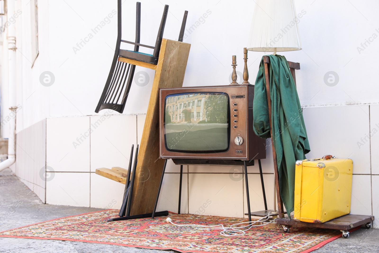 Retro TV on stand and other used stuff near white wall outdoors Photo of Retro TV on stand and other used stuff near white wall outdoors
