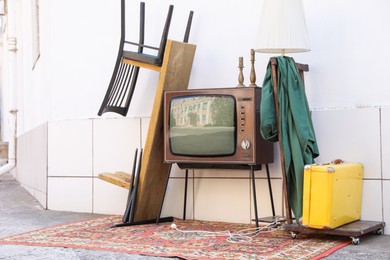 Photo of Retro TV on stand and other used stuff near white wall outdoors