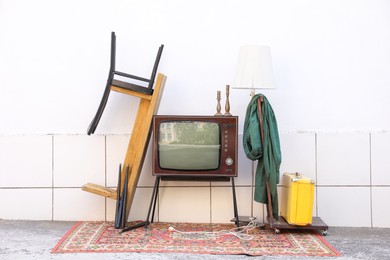 Photo of Retro TV on stand and other used stuff near white wall outdoors