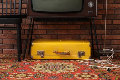 Photo of Retro TV on stand, suitcase and black chair near red brick wall. Used stuff