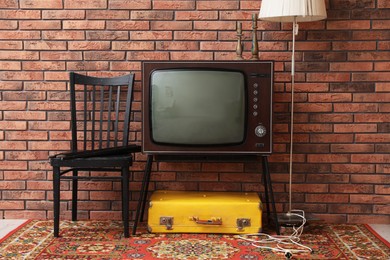 Photo of Retro TV on stand, suitcase, lamp and black chair near red brick wall. Used stuff