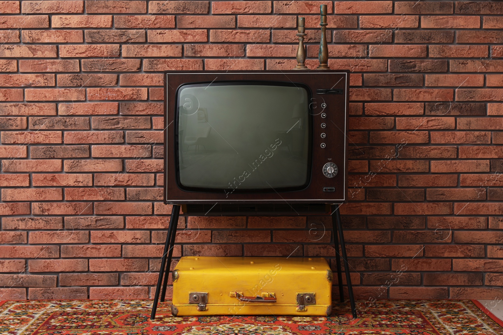Retro TV on stand, suitcase and carpet near red brick wall. Used stuff Photo of Retro TV on stand, suitcase and carpet near red brick wall. Used stuff