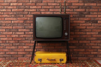 Photo of Retro TV on stand, suitcase and carpet near red brick wall. Used stuff