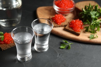 Photo of Cold Russian vodka and sandwiches with red caviar on black table, closeup