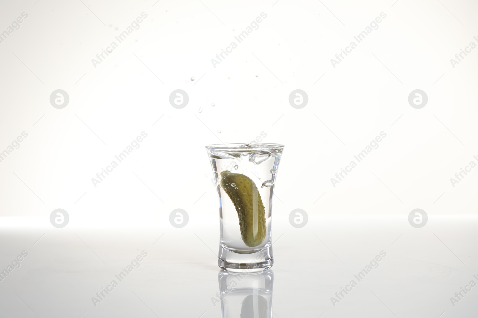 Russian vodka with pickle in shot glass isolated on white Photo of Russian vodka with pickle in shot glass isolated on white