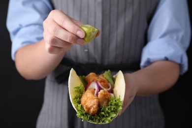 Photo of Woman squeezing lime on fish taco against dark background, closeup