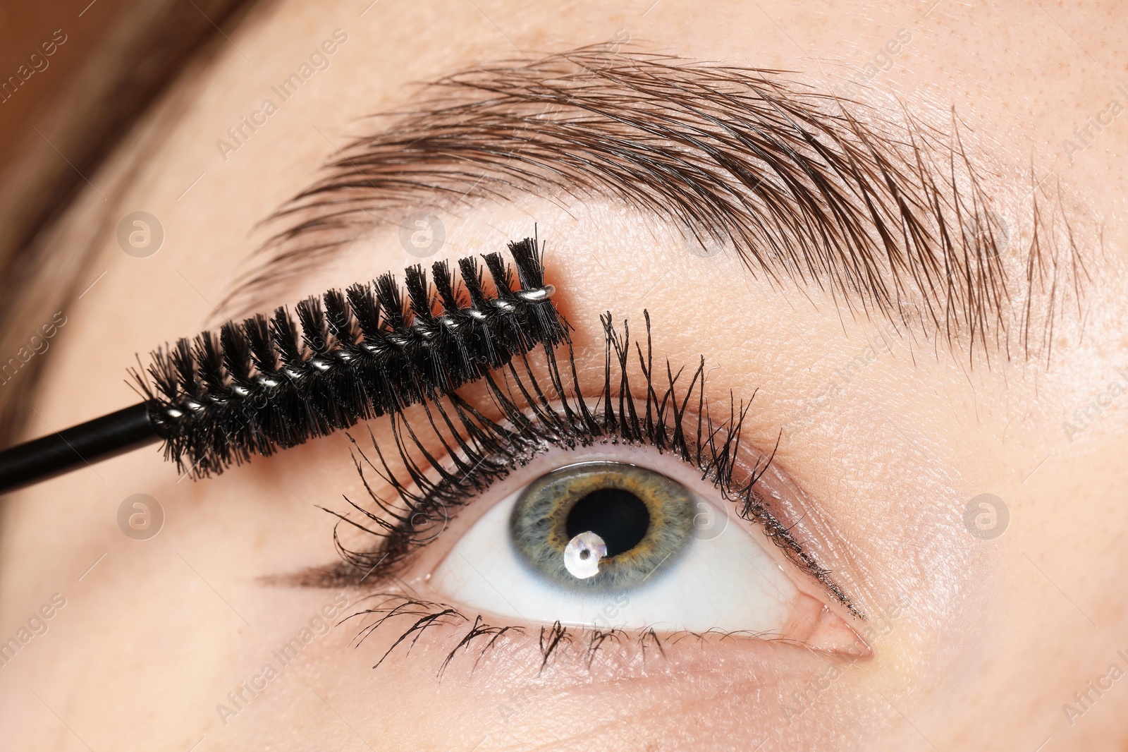 Photo of Woman applying mascara onto her eyelashes, closeup