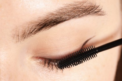 Photo of Woman applying mascara onto her eyelashes, closeup