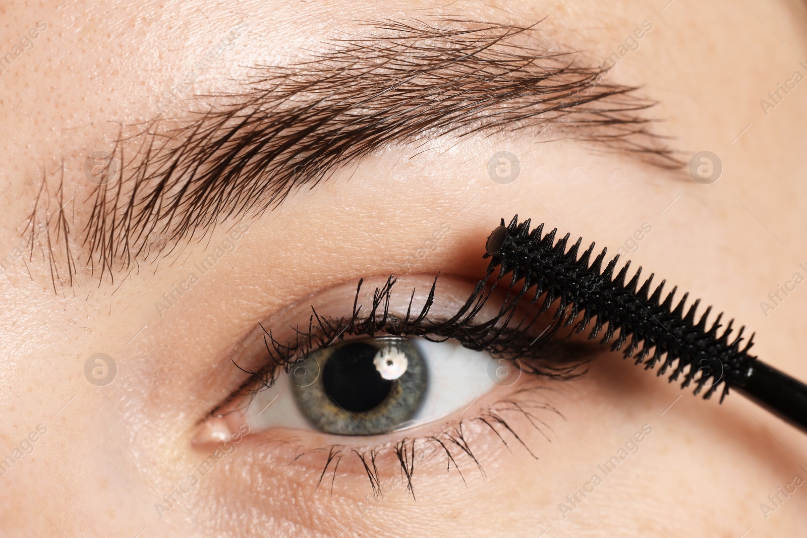 Photo of Woman applying mascara onto her eyelashes, closeup