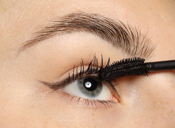 Photo of Woman applying mascara onto her eyelashes, closeup