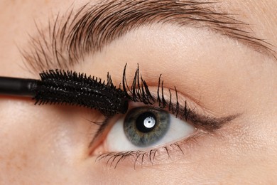 Photo of Woman applying mascara onto her eyelashes, closeup