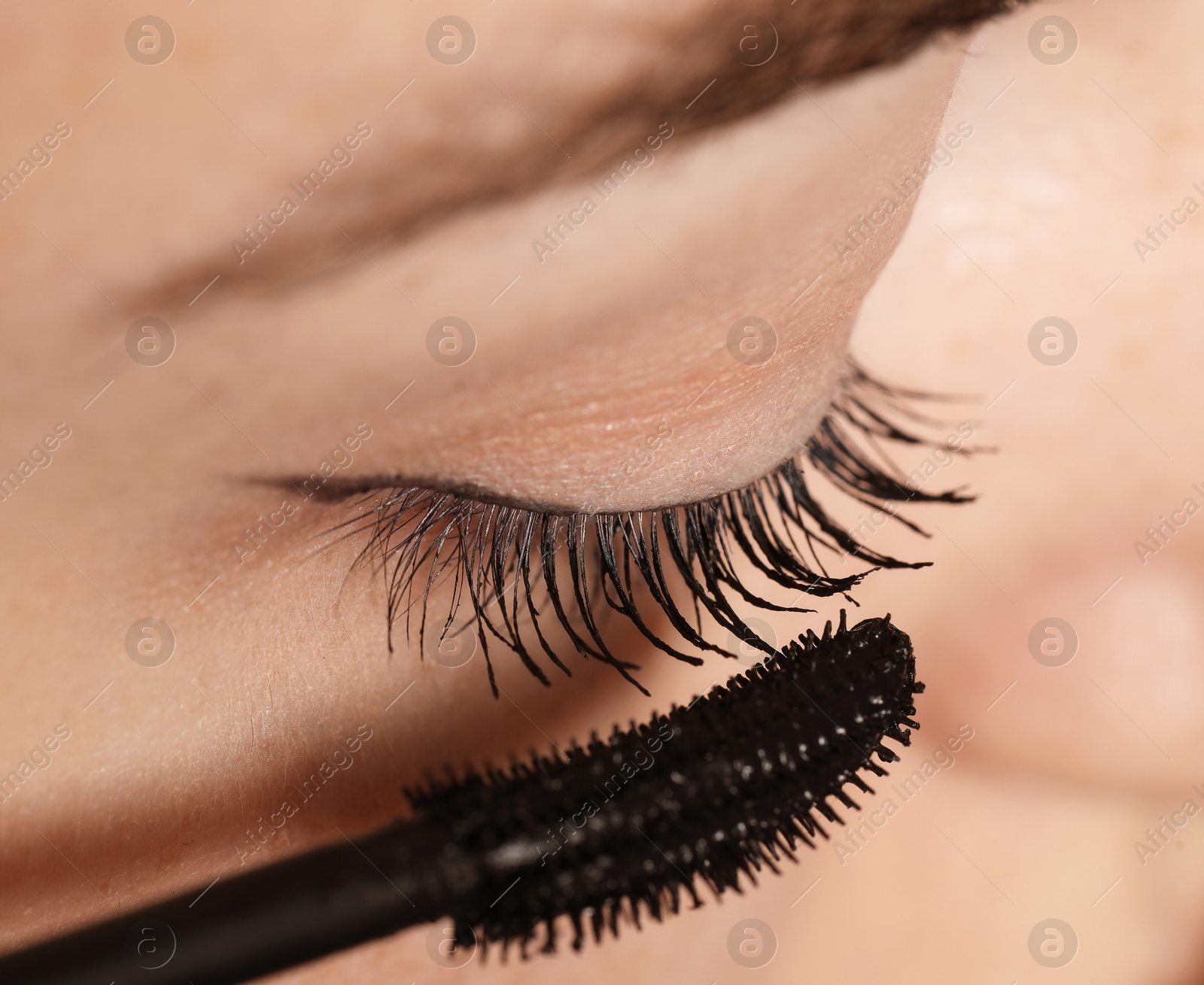 Photo of Woman applying mascara onto her eyelashes, closeup