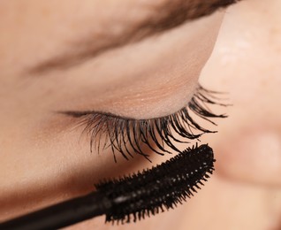 Photo of Woman applying mascara onto her eyelashes, closeup