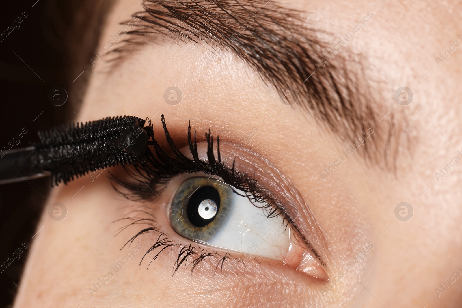 Photo of Woman applying mascara onto her eyelashes, closeup