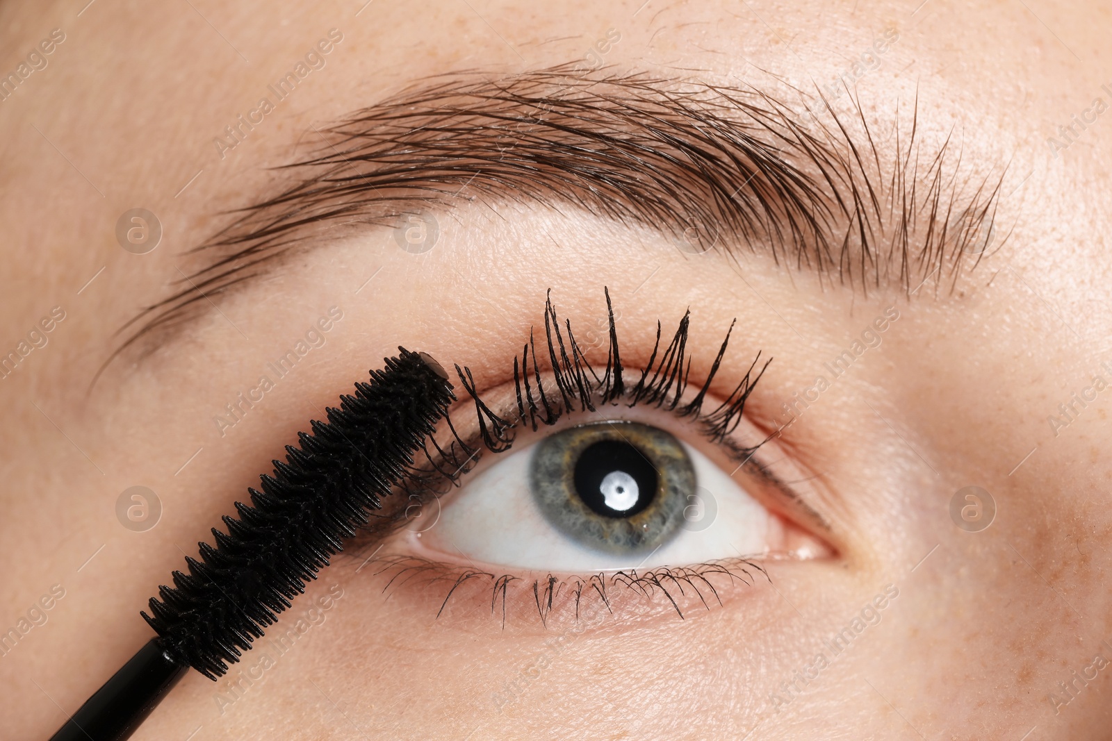 Photo of Woman applying mascara onto her eyelashes, closeup