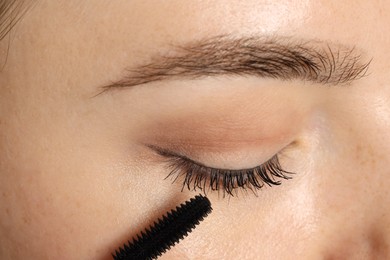 Photo of Woman applying mascara onto her eyelashes, closeup