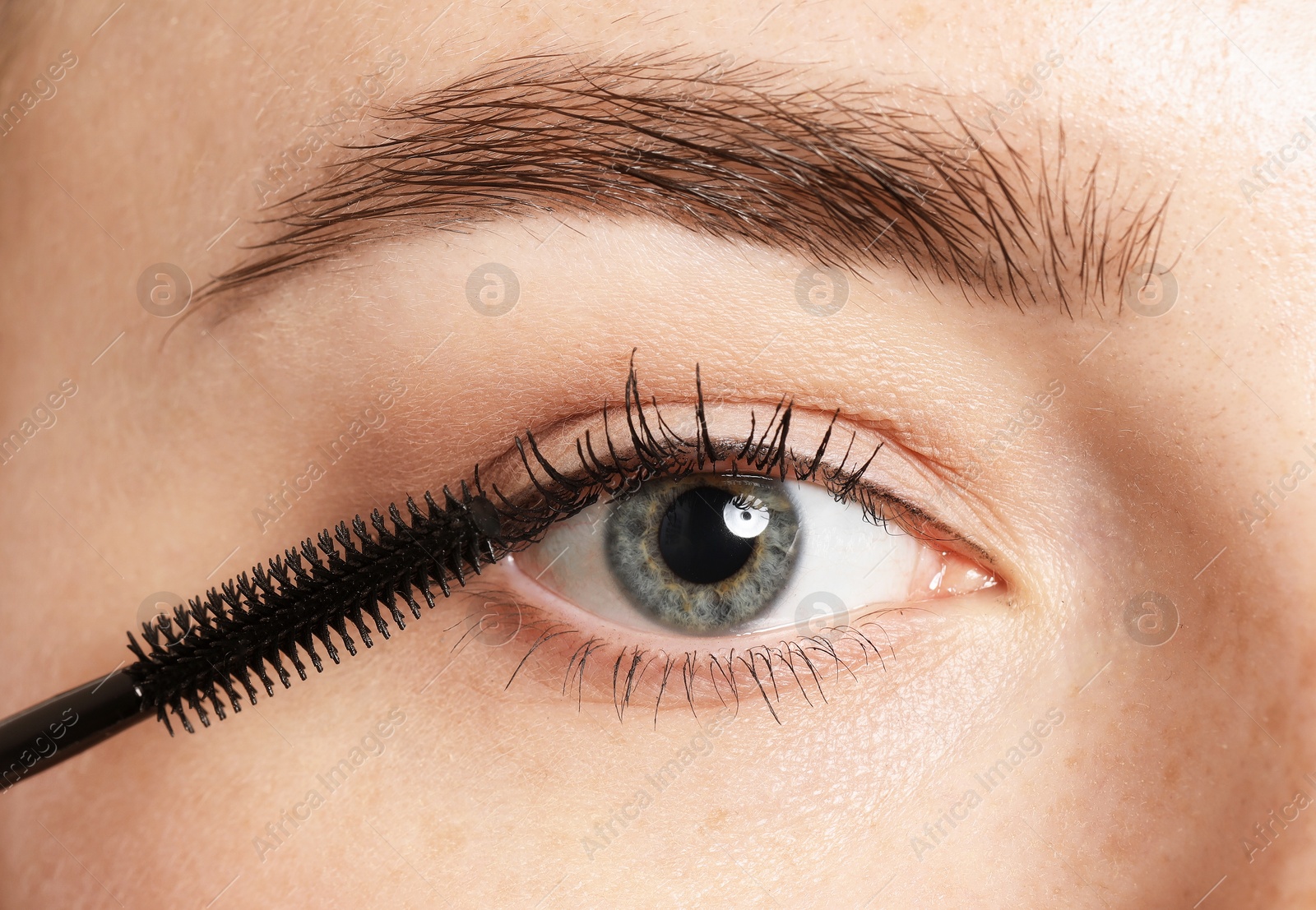 Photo of Woman applying mascara onto her eyelashes, closeup
