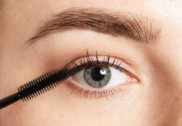 Photo of Woman applying mascara onto her eyelashes, closeup