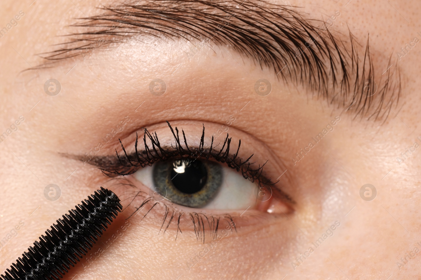 Photo of Woman applying mascara onto her eyelashes, closeup