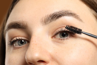 Photo of Woman applying mascara onto her eyelashes on brown background, closeup