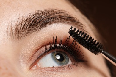 Photo of Woman applying mascara onto her eyelashes on brown background, closeup