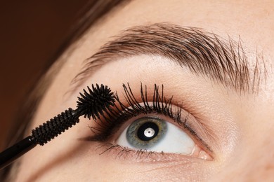 Photo of Woman applying mascara onto her eyelashes on brown background, closeup