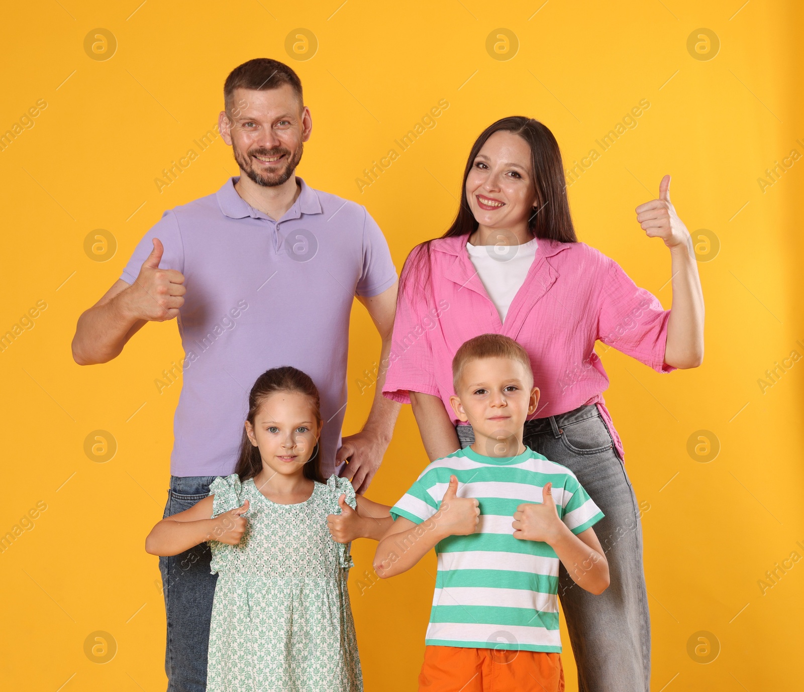 Photo of Happy family showing thumbs ups on yellow background