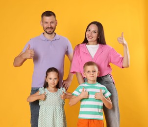 Photo of Happy family showing thumbs ups on yellow background